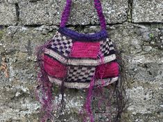 a handbag hanging on a stone wall with purple and pink yarn around the handles