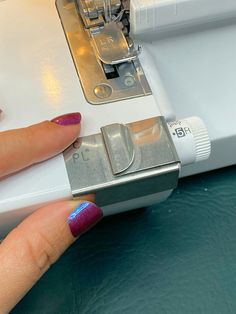 a woman's hand on top of a sewing machine with blue and pink nail polish