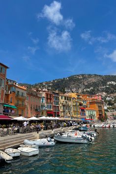 boats are docked in the water next to buildings and umbrellas on a hill side