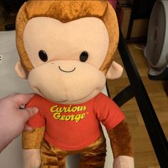 a stuffed monkey wearing a curious george t - shirt is being held by someone's hand