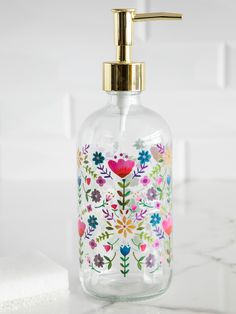 a glass soap dispenser with flowers painted on it