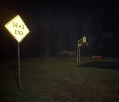 a yellow dead end sign sitting in the middle of a grass covered field at night