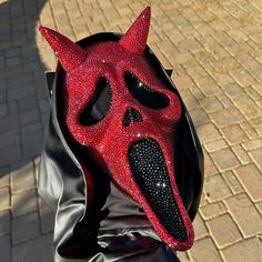 a person wearing a red and black mask with spikes on it's head, sitting in a leather bag