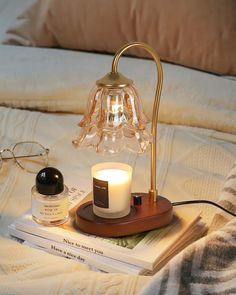 a table lamp sitting on top of a bed next to a candle and some books