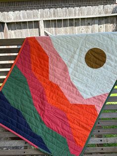 a multicolored quilt hanging on a wooden bench