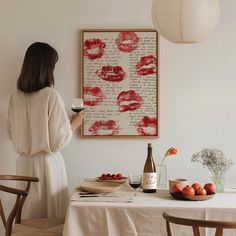 a woman standing in front of a table holding a glass of wine and plate of fruit