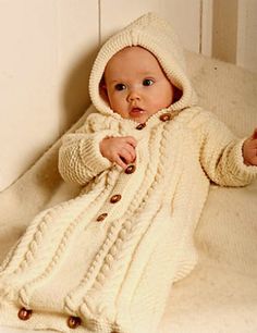 a baby in a white knitted coat laying on a bed with the caption drops design