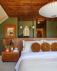 a bed with white sheets and pillows in a bedroom next to a wooden ceiling light