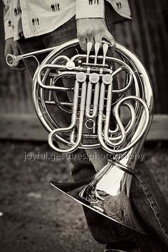 black and white photograph of a man holding a french horn in his hand, outdoors