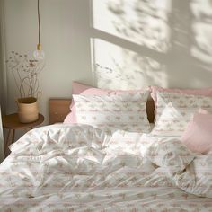 an unmade bed with pink and white comforters in a sunny room next to a window