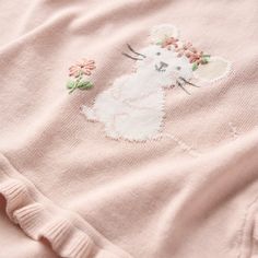 a pink sweater with a cat embroidered on the chest and flowers in the back,