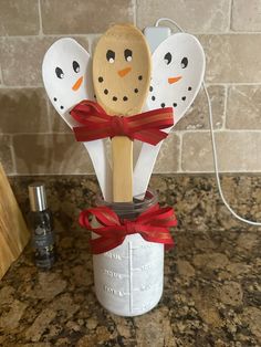 three wooden spoons with snowmen on them are in a mason jar decorated with red ribbon