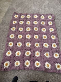 a crocheted blanket with white and yellow daisies on it, sitting on the floor