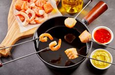 shrimp skewers being cooked in a skillet with dipping sauces on the side