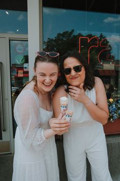 two women standing next to each other holding an ice cream cone in front of a store