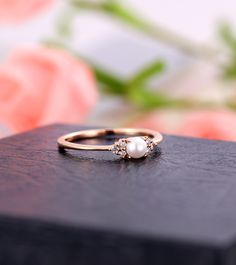 a pearl and diamond ring sitting on top of a wooden box with flowers in the background