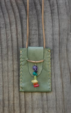 a green leather bag with beads hanging from it's side on a wooden surface