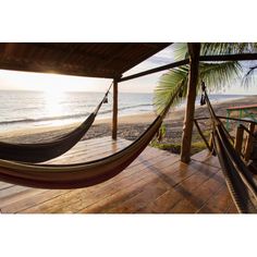 a hammock hanging from the side of a wooden deck next to the ocean