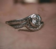 a close up of a ring on a bed with a diamond in the center and an intricate band around it