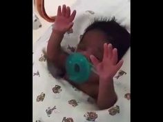 a baby is laying in bed with his hands up to the camera and holding a green object