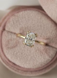 an engagement ring with a cushion - cut diamond sits on top of a pink velvet box