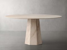 a round table with a wooden base on a concrete flooring surface in front of a gray wall