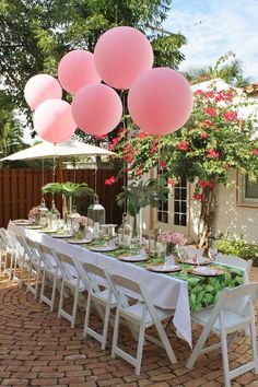 the table is set with pink balloons and white linens for an outdoor dinner party