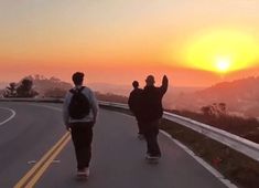 two skateboarders are walking down the road as the sun sets in the background