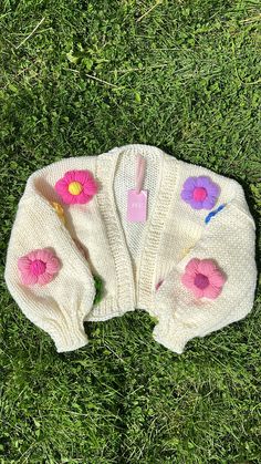 three knitted sweaters with flowers on them laying in the grass next to a toothbrush