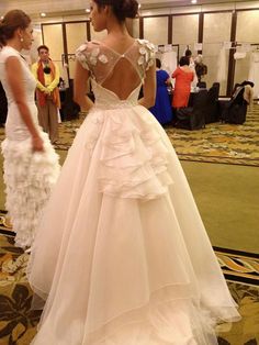 a woman in a white wedding dress standing next to another woman wearing a gown with ruffles on it