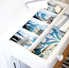 an open drawer with silverware and spoons in it on top of a table