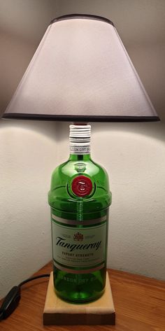 Beautiful abat-jour made with Tanqueray gin bottle on natural beech wood support. The lampshade is in gray fabric, the E27 lamp holder is wired with switch. The plug is Italian 10A. Decorate your room, living room or office desk with this original lamp that will give a touch of uniqueness to your environment! Wide availability of bottles! Ask if there is your favorite and I will make it just for you! If you like the item but prefer a different size or color or you have something special in mind, Jager Bottle Lamp, Gin Tanqueray, Bottle Table Lamps, Tanqueray Gin, Liquor Bar, Gin Bottle, Bar Man Cave, Gin Bottles, Bottle Lamp