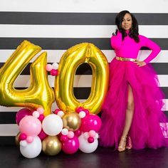 a woman in a pink dress standing next to balloons and the number 40 sign that says'50 '