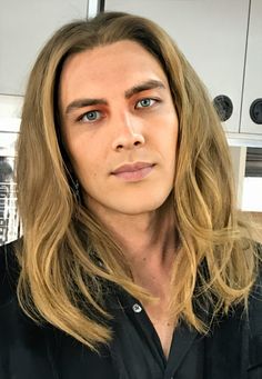 a man with long hair and blue eyes in a black shirt looking at the camera