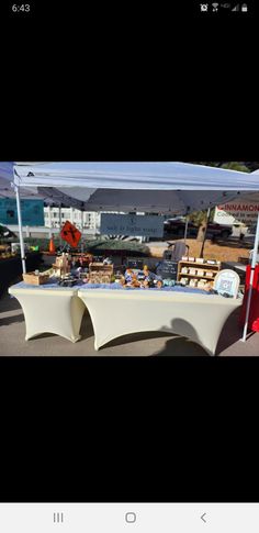 a white table topped with lots of food under a tent on top of a parking lot