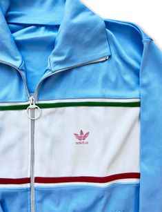 Adidas track jackets are highly sought after by collectors due to their unique design, limited availability, and historical significance. With iconic Adidas logo and stripes the retro graphics harken back to the style Farrah Fawcett wore on the tennis court and golf course. This one is rare due to it's gorgeous sky blue color and amazing collar. We love the red and green stripe accents; this jacket would go with anything! Also popularized by the hip-hop group, the Beastie Boys, in the 1980s. Their iconic style reflects the group's rebellious and eclectic musical style, and is still popular among fans and collectors today. FABRIC: Polyester Condition: Faded Red adidas logo, white portion of jacket slightly dingy; no visible stains or marks. SIZE: Large womens | Medium Mens Sporty Blue Track Jacket With Three Stripes, Retro Track Jacket With Three Stripes, Vintage Three Stripes Track Jacket For Sports, Vintage Track Jacket With Three Stripes For Sports, Retro Long Sleeve Track Jacket With Three Stripes, Retro Streetwear Track Jacket With Three Stripes, Retro Track Jacket With Three Stripes For Streetwear, Vintage Adidas Jacket, Sky Blu