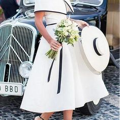 a woman in a white dress and hat is standing next to an old fashioned car