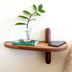 a wooden shelf with a plant and books on it next to a laptop, cell phone or tablet