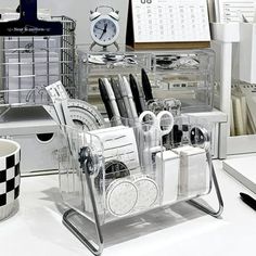 an office desk with various pens and pencils in a clear holder next to a clock