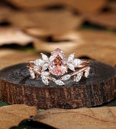 a pink diamond ring sitting on top of a piece of wood with leaves around it