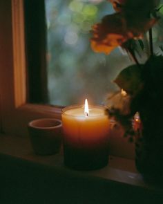 a lit candle sitting on top of a window sill next to a vase filled with flowers