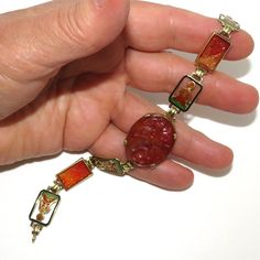 A vintage art deco style Asian inspired 14 K gold bracelet with carved carnelian panels and enamel Buddhas. The bracelet is 19.5 cm long and has a spring ring clasp. It is marked with an unclear makers mark and "14 K". The bracelet features an oval center gold framed carved carnelian panel with a bird and flower design that measures 2.7 by 2.2 cm. It has two smaller 1 by 1.5 cm rectangular links carved with  matching bird and flower designs, and four rectangular links featuring a cutout Buddha in carnelian colored enamel seated on a green base surrounded by a black frame. The bracelet is in excellent condition. A nice example of art deco period Asian inspired design! Carved Carnelian Vintage Jewelry, Vintage Carnelian Bracelets As Gift, Vintage Carnelian Bracelets Gift, Vintage Carnelian Bracelet Gift, Vintage Carved Carnelian Jewelry, Vintage Enamel Jewelry With Rectangular Shape, Vintage Rectangular Enamel Jewelry, Elegant Bakelite Bracelet Jewelry, Elegant Bakelite Bracelet