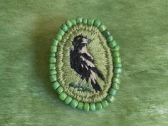 a green beaded brooch with a black bird on it's back side