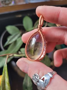 a hand holding a wire wrapped pendant with a large tear shaped stone in the center