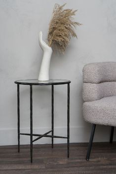 a white vase sitting on top of a table next to a gray chair and wall