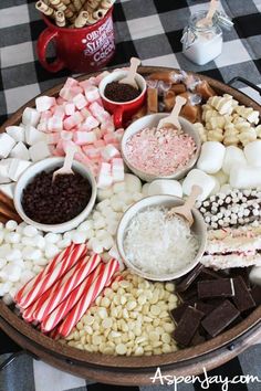 a platter filled with marshmallows, chocolate and candy canes on a checkered table cloth