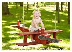 a toddler sitting on a red wooden swing set in the park with his feet up