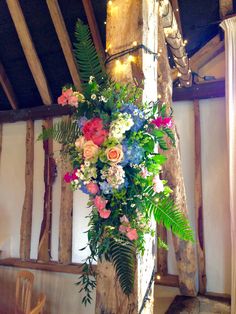 an arrangement of flowers and greenery is hanging from a wooden pole in the middle of a room