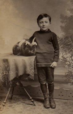 an old photo of a young boy standing in front of a table with a cat on it