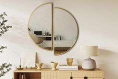 a round mirror on the wall above a dresser with a lamp and vase in front of it